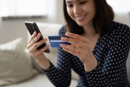 Crop close up of happy Asian millennial girl hold plastic credit card make payment or purchase on...