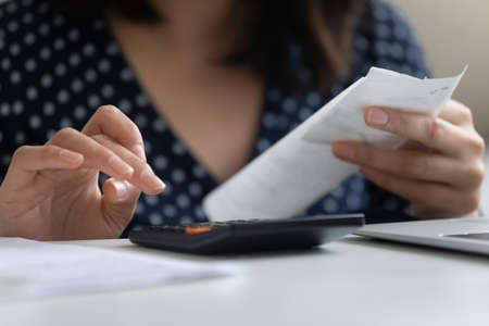 Crop close up of young woman calculating family household expenses expenditures using calculator...
