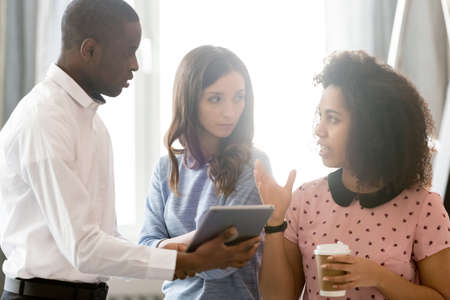 Diverse colleagues employees discussing online project during coffee break, using computer tablet,...