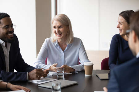 Multi ethnic cheerful workmates laughing during group briefing in office. Millennial mature partners negotiating having friendly relations feels happy, successful effective meeting accomplish conceptの写真素材