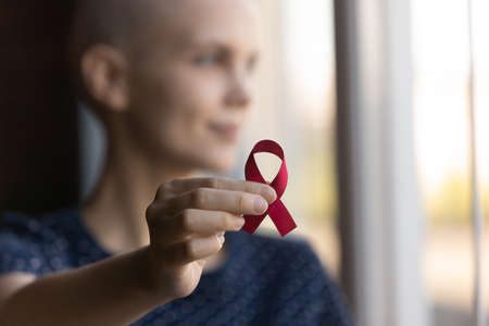 Crop close up of sick woman hold red ribbon symbol of oncology show support and awareness of disease, ill female cancer patient feel supportive about people with illness, recovery, healthcare conceptの写真素材