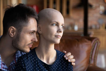 Loving young Caucasian husband hug support sick cancer patient hairless wife, look in distance dream...