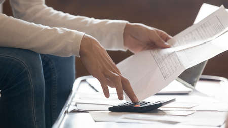 Close up focused young woman holding paper payment taxes documents, calculating economical monthly expenditures alone indoors, managing household finances, domestic savings investment concept.の写真素材