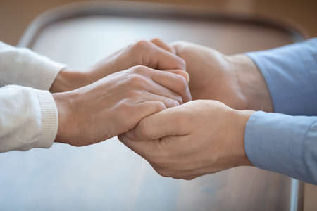 Close up young man holding hands of wife, giving psychological support, asking for forgiveness, making peace after quarrel, affectionate couple showing love care devotion, reconciliation moment.の写真素材