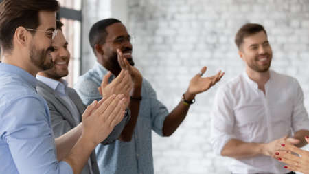 Excited diverse employees clapping hands, applauding and cheering, celebrating business achievement, sharing success, congratulating colleague with promotion, standing in modern officeの写真素材