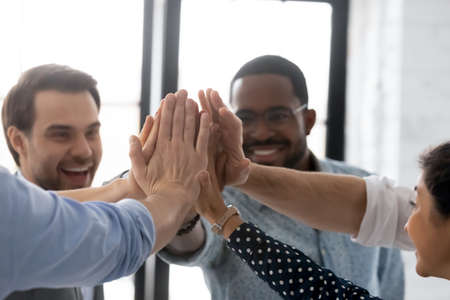 Close up diverse business people joining hands, giving high five at corporate meeting, celebrating...