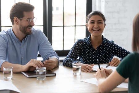 Happy diverse business people laughing at corporate meeting, sitting at table in boardroom, business partners enjoying conversation, discussing project statistics or strategy, teamwork conceptの写真素材