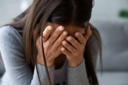 Close up unhappy young woman hiding face in hands, feeling desperate cheated hopeless alone indoors....