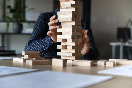 Close up young indian woman constructing tower with wooden bricks alone in office, sitting at table. Female employee manager developing strategic thinking skills or challenging at workplace.の写真素材