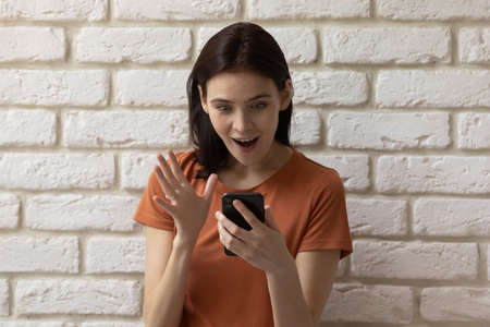 Excited stunned millennial girl look at cellphone screen shocked by unexpected sale deal or discount offer, amazed young woman surprised by unbelievable message on smartphone, luck conceptの写真素材