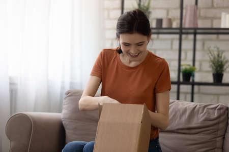 Happy young Caucasian woman unpack cardboard box internet order at home, shopping online on web,...