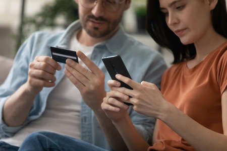 Crop close up of young couple make online purchase payment on cellphone pay with credit card, millennial man and woman shopping on internet on smartphone, use secure banking service system on gadgetの写真素材