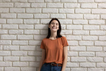 Portrait of positive millennial Caucasian girl teenager isolated on white brick wall look at camera smiling, happy young woman tenant or renter feel optimistic overjoyed, show white healthy teethの写真素材