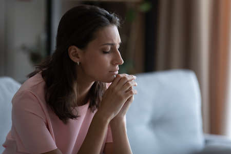 Unhappy distressed young Arabic indian woman sit on sofa at home thinking pondering, upset depressed arab mixed race female mourn yearn in living room, feel stressed with abortion miscarriage problemsの写真素材