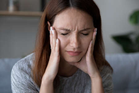 Close up of exhausted young red-haired woman suffer from headache or migraine at home, tired female...