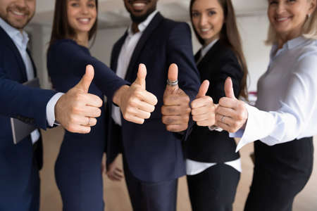 Close up portrait of smiling diverse business partners or colleagues standing close together showing thumbs up gesture recommending customers best goods or service, being happy and proud of teamworkの写真素材