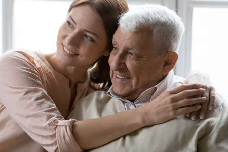 Affectionate young woman cuddling loving positive older retired daddy, dreaming together indoors or...