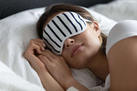 Close up peaceful young woman wearing stripped mask sleeping on side, resting on soft pillow under...