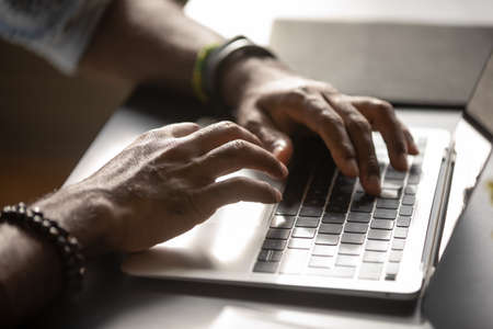 Close up male hands typing on laptop keyboard, African American man working online, blogger preparing new post for blog, businessman writing financial report or email, using computer appsの写真素材