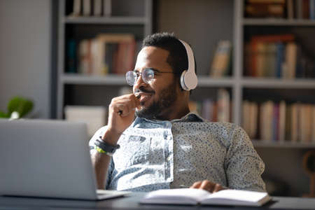 Dreamy smiling African American man wearing headphones looking to aside, dreaming about good future,...