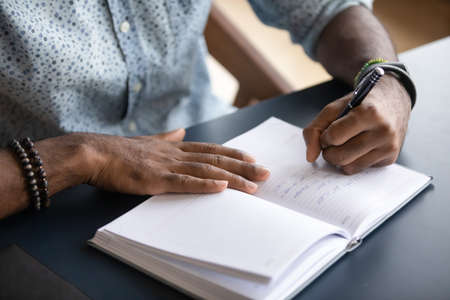 Close up African American businessman writing important information in notebook, planning workday,...