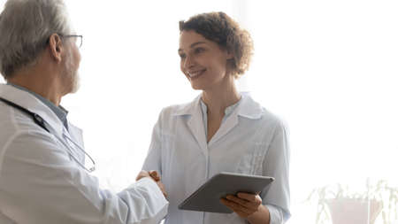 Mature doctor executive shaking smiling nurse hand, thanking for good work result, reward, happy...