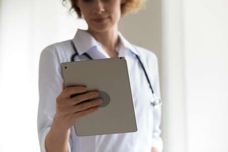 Close up focused woman professional doctor holding digital tablet, looking at screen, serious therapist physician gp working online, analyzing patient medical checkup results, telemedicineの写真素材
