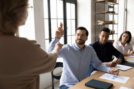 Initiative interested young businessman in eyeglasses raising hand, asking questions about marketing...