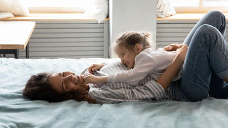 Happy affectionate young mommy lying with little baby girl daughter on comfortable bed, enjoying lazy weekend morning time at home. Bonding two generations family relaxing together in bedroom,の写真素材