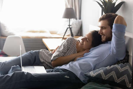Peaceful young couple resting on cozy bed, watching romantic movie online on computer. Happy...