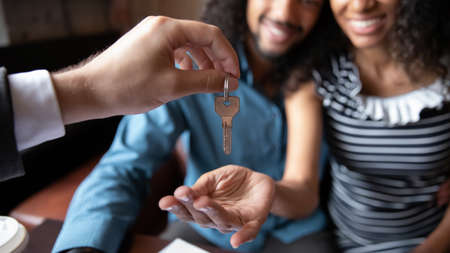 Close up happy young African American couple receiving keys from realtor, real estate agent, overjoyed family husband and wife purchasing first apartment, buying new house, making deal at meetingの写真素材