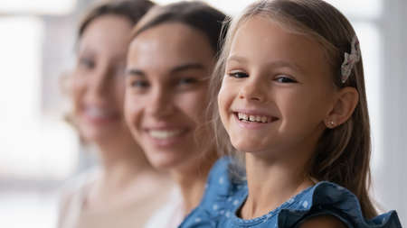 Close up headshot portrait of happy cute little 7s old girl with beautiful millennial mother and smiling older senior grandma. Cheerful different female generations family looking at camera indoors.の写真素材