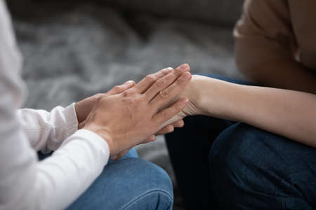 Close up young woman holding hands of elderly retired mother, enjoying sincere conversation, sharing secrets or asking for forgiveness indoors. Loving caring multigenerational family making peace.の写真素材