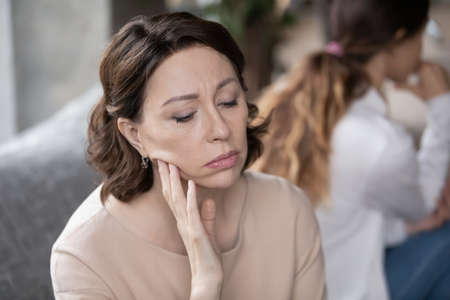 Stressed 60s mature woman feeling offended after quarrel with grown up daughter, ignoring each other, sitting on couch in silence. Unhappy different generations family having communication problems.の写真素材