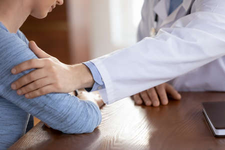 Close up caring doctor therapist touching upset frustrated female patient hand at medical appointment, physician gp comforting depressed young woman at meeting, psychological help conceptの写真素材