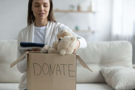 Kind young woman putting belongings into carton box, donating things to homeless or children orphans. Compassionate altruistic millennial volunteer taking part in charity activity, recycling concept.の写真素材