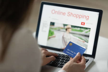 Close up young woman involved in online shopping on laptop. Happy millennial girl making purchases in popular internet store, entering information or cvv code from plastic banking credit debit card.の写真素材