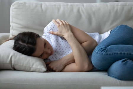 Stressed young woman lying on sofa, embracing shoulders with arms, suffering from depression alone...