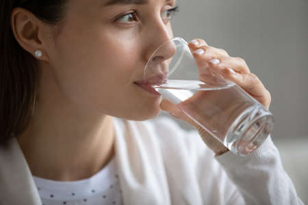 Side close up head shot view happy pleasant young woman enjoying drinking water indoors. Positive...