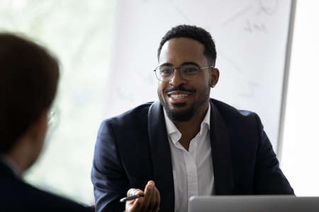 Smiling African American young businessman in glasses talk with business partner at office meeting. Happy motivated biracial man boss or CEO have talk, discuss cooperation with colleague at briefing.の写真素材