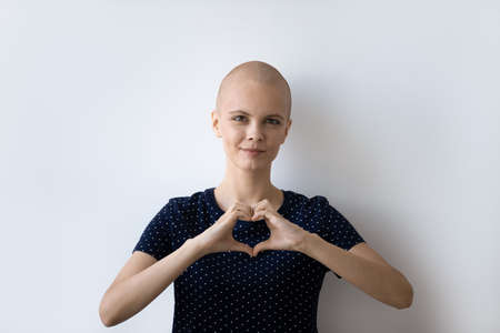 Headshot portrait of young hairless sick woman suffer from cancer show heart love hand sign or...