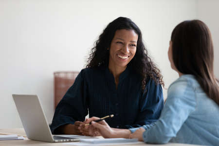 Smiling African American businesswoman talking to colleague, diverse employees brainstorming,...