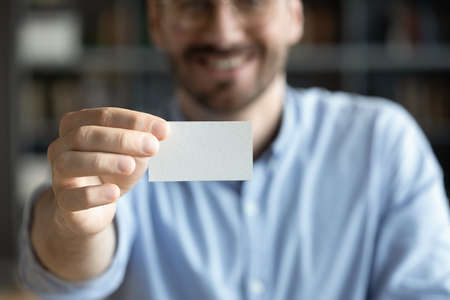 Close up of smiling Caucasian businessman stretch hand show empty blank white mockup business card to client at meeting. Happy male employee introduce get acquainted greeting with partner.の写真素材