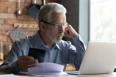 Stressed elderly grey-haired man in glasses look at laptop screen have problems paying bills taxes...