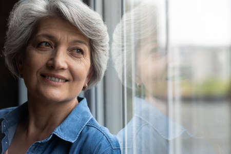 Close up of dreamy elderly Caucasian grey-haired woman look in window distance thinking or visualizing. Happy mature 60s female lost in thoughts, dreaming or imagining bright healthy future.の写真素材