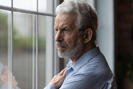 Unhappy old Caucasian grey-haired man look in window distance thinking or missing good past days....