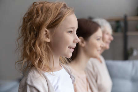 Close up side view three generations of women standing in row at home, smiling pretty little girl profile portrait with young mother and mature grandmother, family posing for photoの写真素材