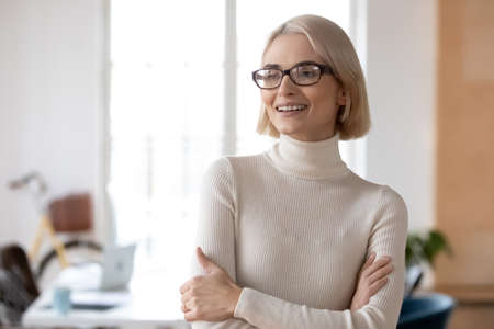 Smiling millennial Caucasian woman worker look in distance thinking dreaming of career success or promotion. Happy young businesswoman in glasses visualize new opportunities. Business vision concept.の写真素材