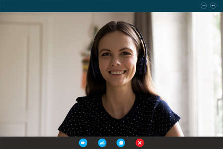 Close up headshot screen view portrait of smiling millennial female in headphones speak talk on video call. Happy Caucasian woman have webcam virtual conference or online web lesson, study distant.の写真素材