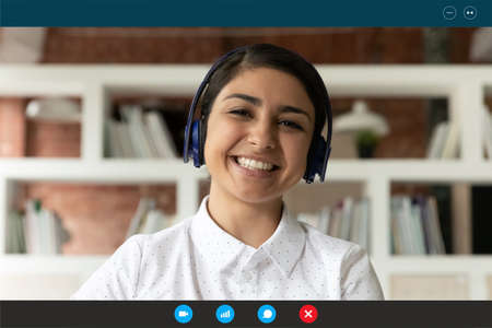 Close up screen view portrait of smiling Indian woman in headphones talk on video call at home....